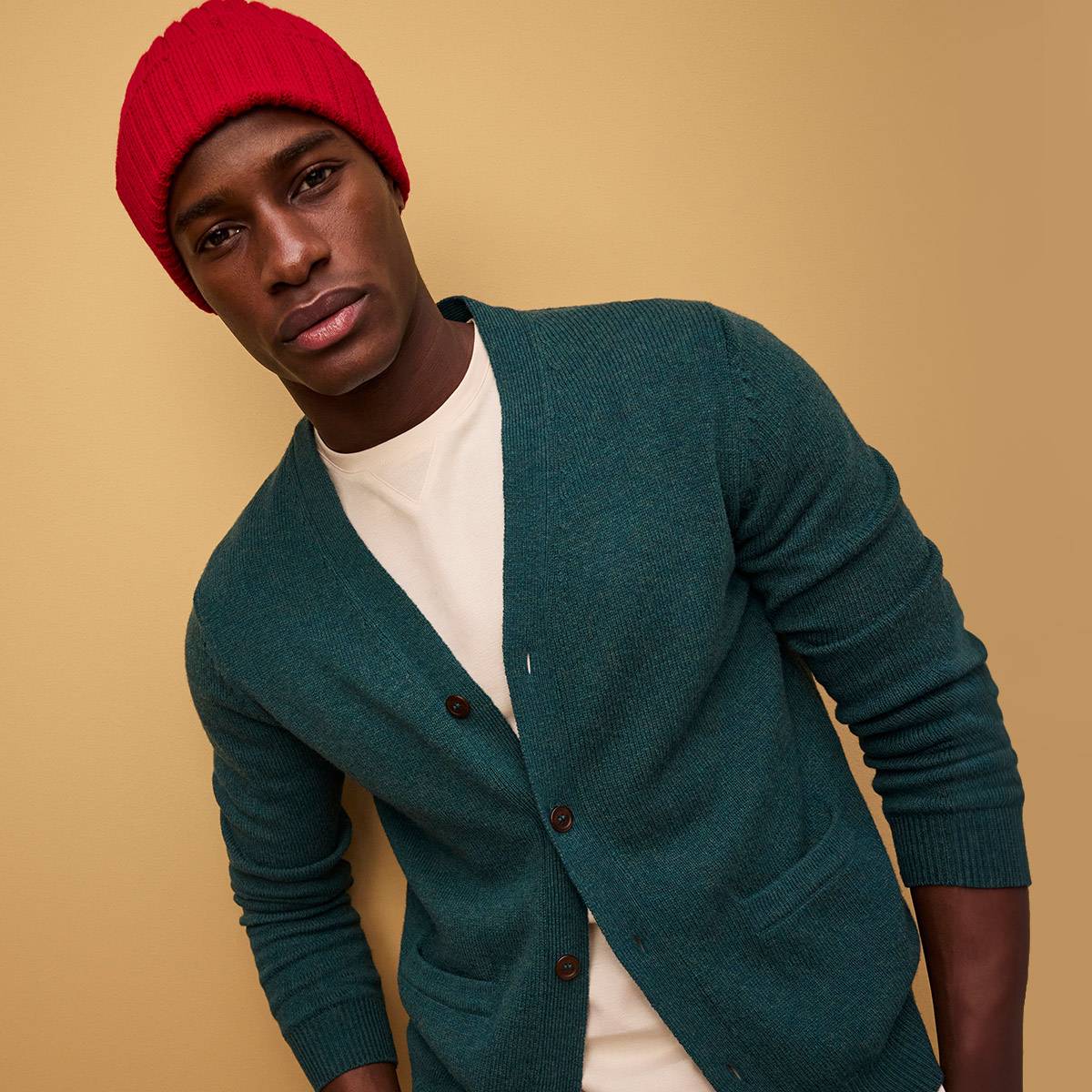 Man wearing green cardigan, white T-shirt, beige chinos and red beanie. Shop gifts for him